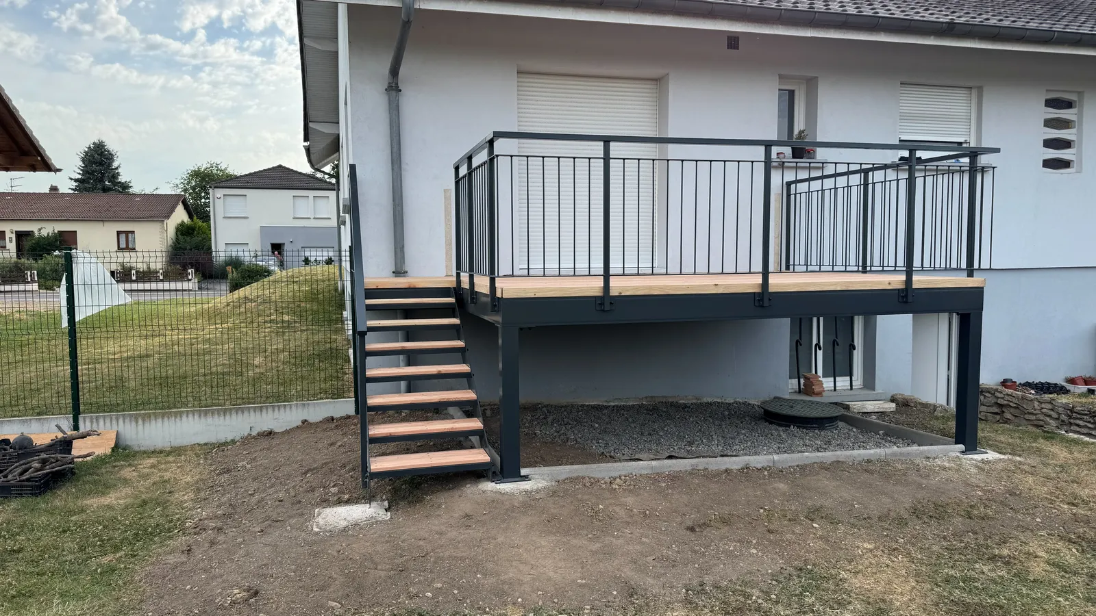Terrasse sur pilotis à Roupeldange — ossature acier anthracite, platelage douglas et escalier d'accès au jardin